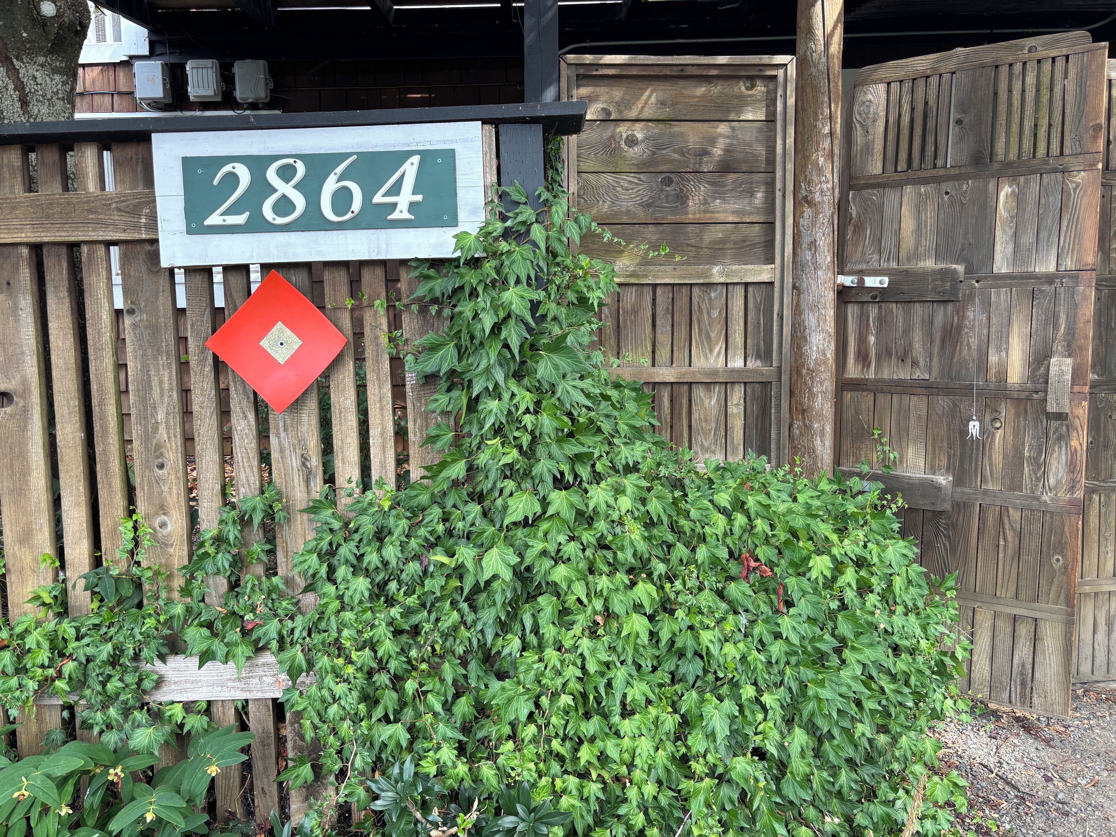 A wooden fence with a house number sign and a red diamond-shaped sign.