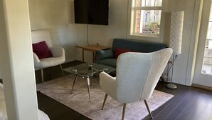 A living room with a sofa, armchair, coffee table, and a flat-screen TV mounted on the wall. - Centrally located private studio in Chemainus (Chemainus)