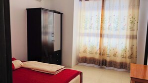 Un dormitori amb un llit, un armari i una finestra amb cortines florals.