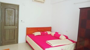 Habitació amb un llit individual, un panell de capçal de fusta, un llençol de llit vermell i blanc, i un armari de fusta.