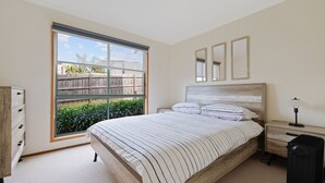 Une chambre avec une grande fenêtre, un lit avec une literie à rayures, une table de chevet avec une lampe et une tête de lit en bois.