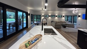 Une cuisine moderne avec un plan de travail en marbre, un saladier en bois rempli de collations et un coin repas avec une table et des chaises.