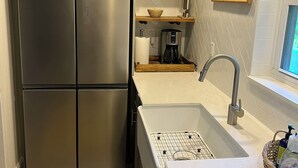 Et moderne køkken med rustfrie apparater, hylder i træ, en hvid flisevæg og et stort vindue.