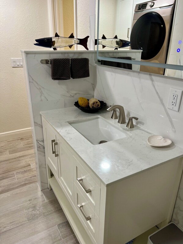 A modern bathroom with a marble sink, a built-in washing machine, and a black shelf with decorative items.