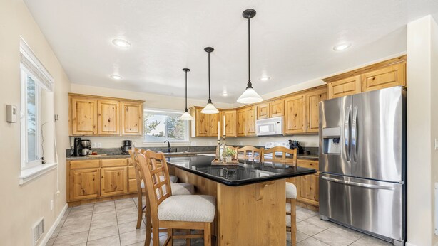 A kitchen with wooden cabinets, a stainless steel refrigerator, and a central island with chairs. - Yellowstone Adventure-Island Park (Island Park)