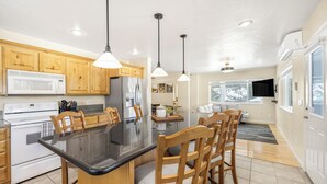 A modern kitchen with wooden cabinets, a black countertop, and a central island with chairs. - Yellowstone Adventure-Island Park (Island Park)