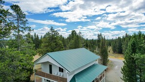 A two-story house with a green roof, surrounded by dense forest, and a clear sky. - Yellowstone Adventure-Island Park (Island Park)