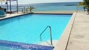 A rectangular swimming pool with a metal ladder, surrounded by a concrete deck. - Beach front apartment with spectacular views.
 (Juan Dolio)
