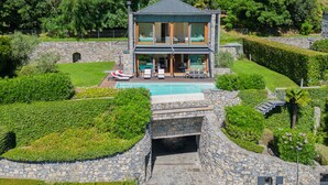 Ein modernes, zweistöckiges Haus mit Swimmingpool, Steinwänden und üppiger Bepflanzung.