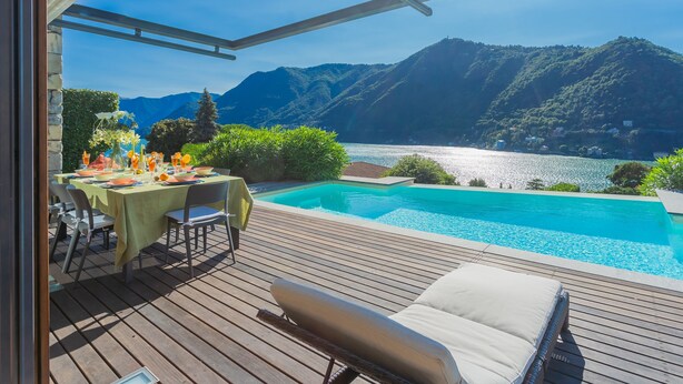 Eine Holzterrasse mit Pool, Essbereich im Freien und Blick auf einen See und Berge.