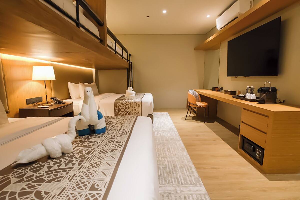 Ein Hotelzimmer mit Etagenbett, Schreibtisch, Flachbildfernseher, Kaffeemaschine und Minibar.