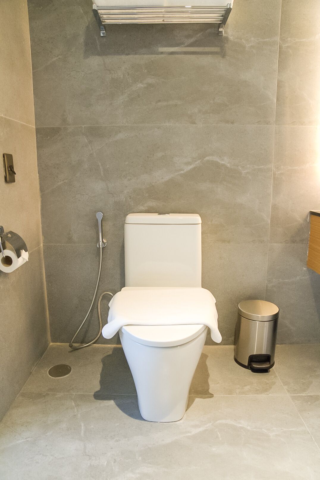 A modern bathroom with a white toilet, a handheld showerhead, and a trash can.