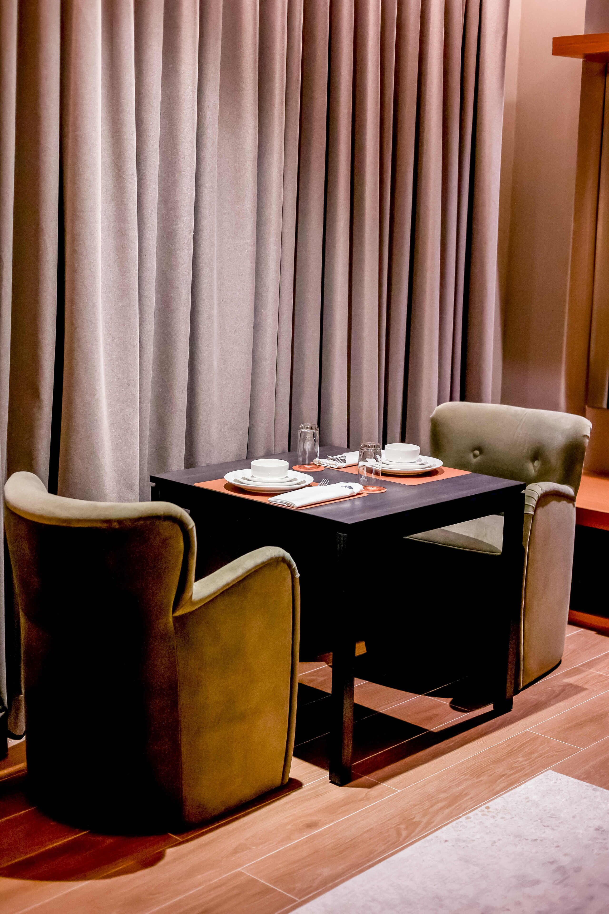A dining area with a table set for two, two chairs, and a curtain backdrop.
