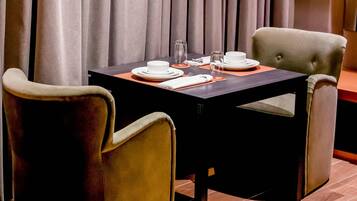 A dining area with a table set for two, two chairs, and a curtain backdrop.