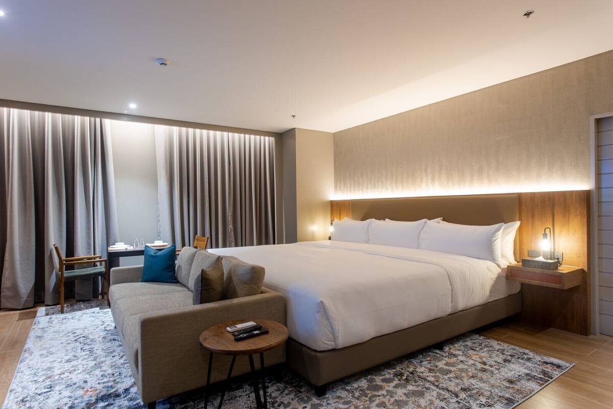 Ein modernes Hotelzimmer mit einem großen Bett, einer Couch, einem kleinen Tisch und einem Schreibtisch.