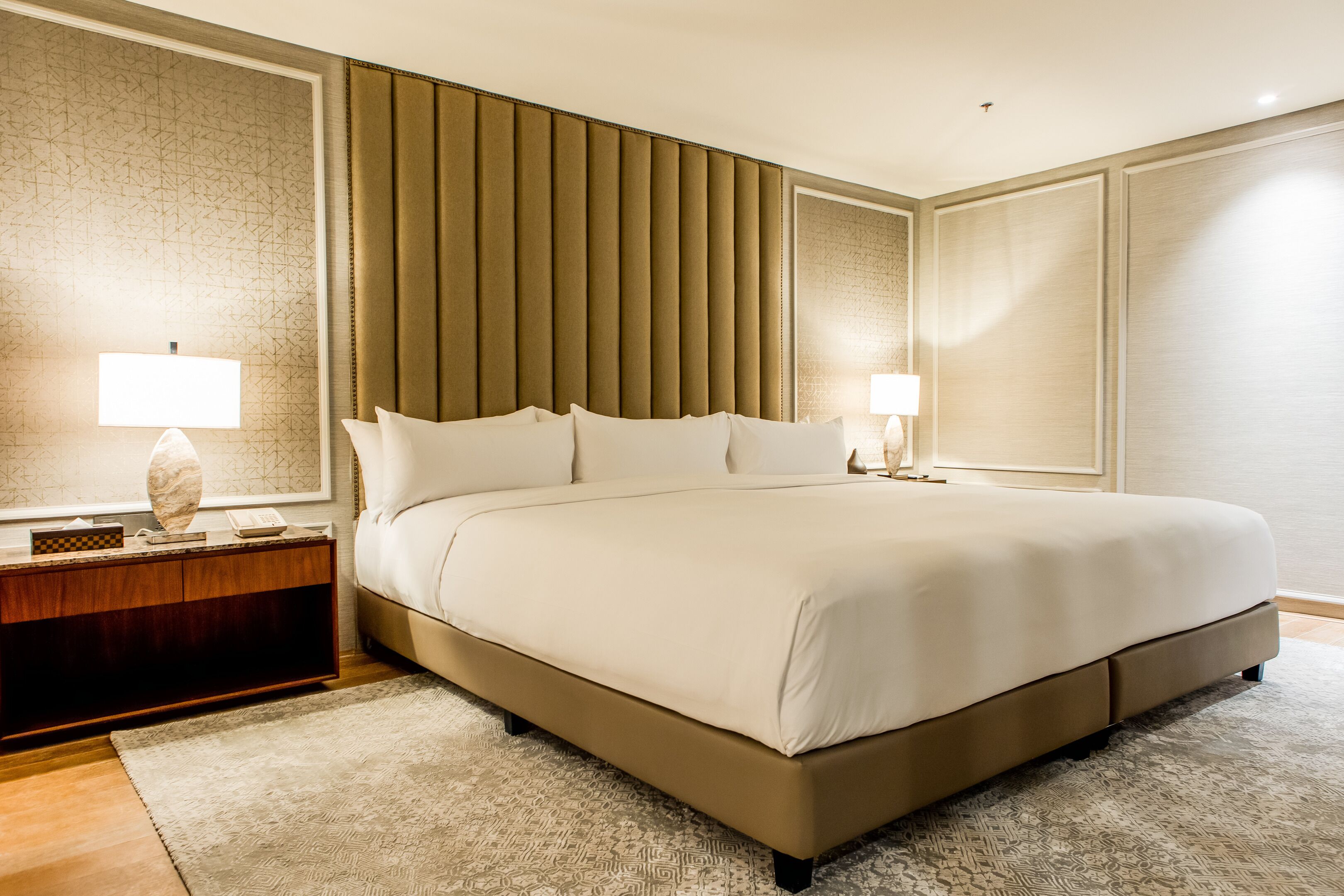 A large bed with a headboard, a bedside table with a lamp, and a patterned rug.