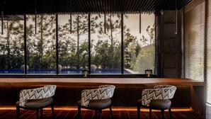 A modern bar area with three patterned chairs and a large window overlooking a garden. - Brittany Hotel Villar City (Bacoor City)