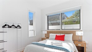Un dormitorio ordenado con cama, mesitas de noche, ventana y perchero.