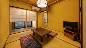 A traditional Japanese room with tatami flooring, a low wooden table, a television on a wooden stand, and a sliding shoji door with a view of the outside. - Kanade Sanjusangendo (Kyoto)