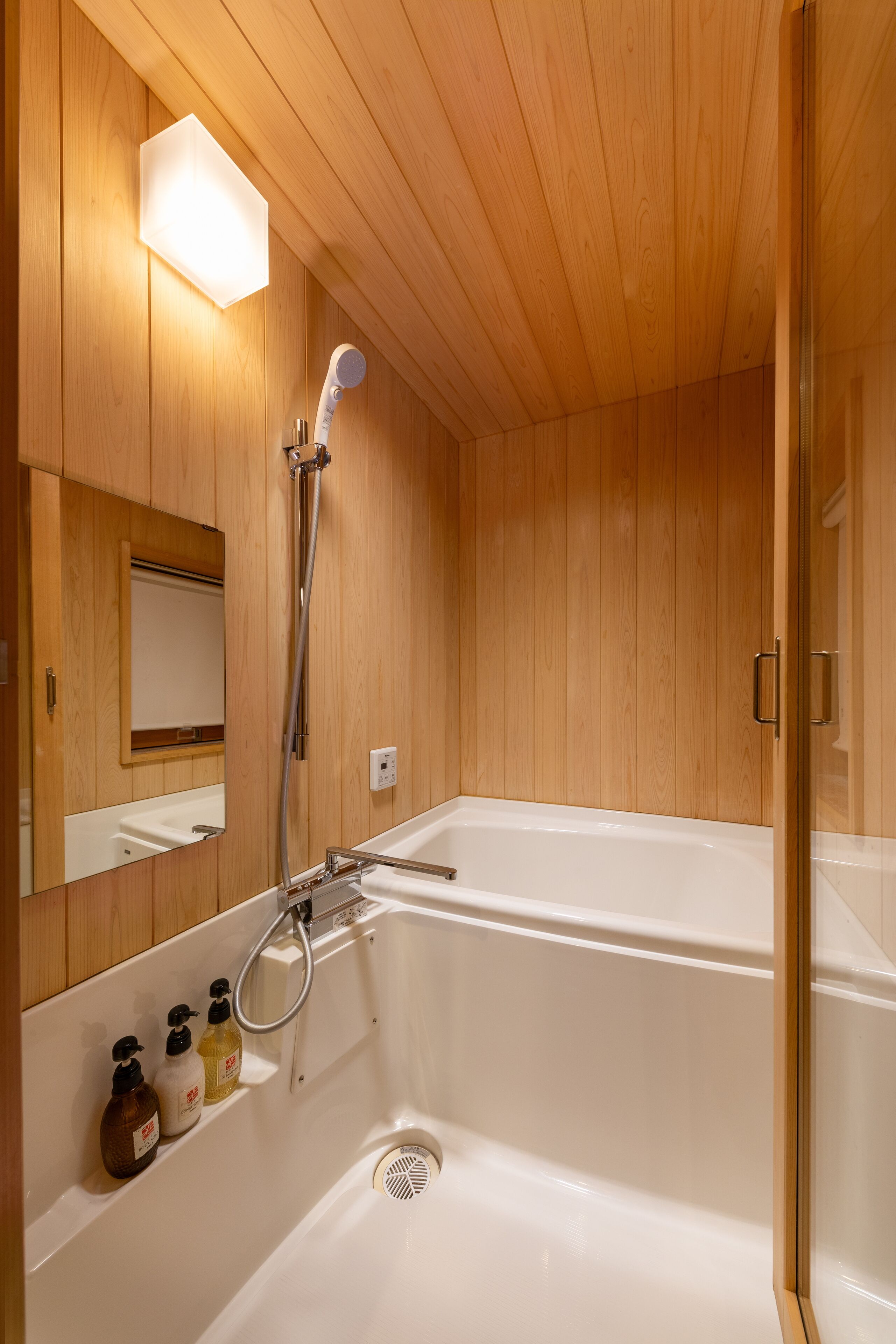 Een betegelde badkamer met een bad, een douche en een spiegel.