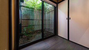 A room with a sliding glass door leading to a backyard with a wooden fence and greenery. - Kanade Sanjusangendo (Kyoto)