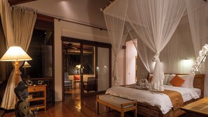 Un dormitorio con una cama de madera, un banco, una estatua y un espejo grande.