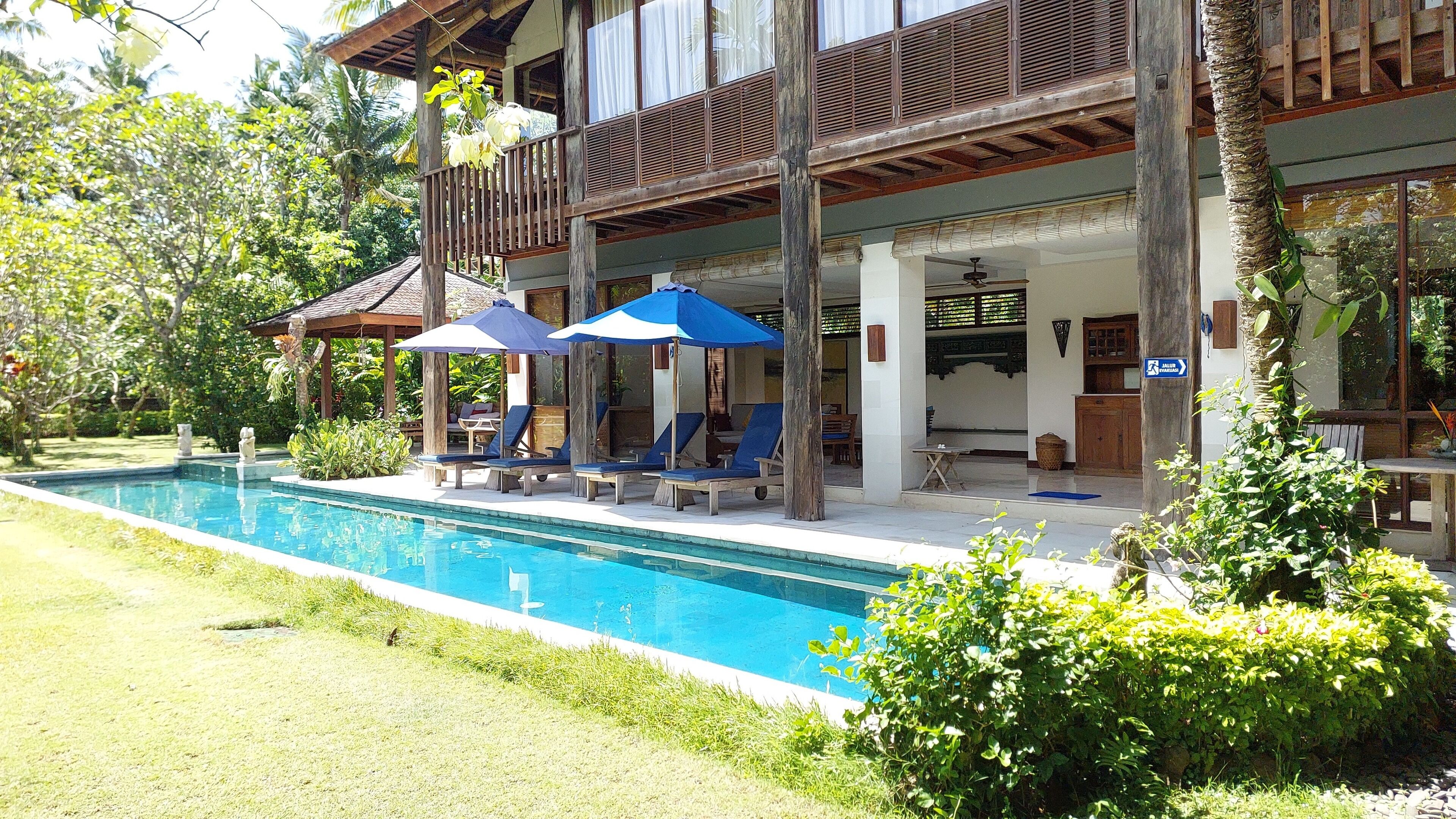 A poolside area with lounge chairs and umbrellas, a wooden deck, and a building with a balcony.