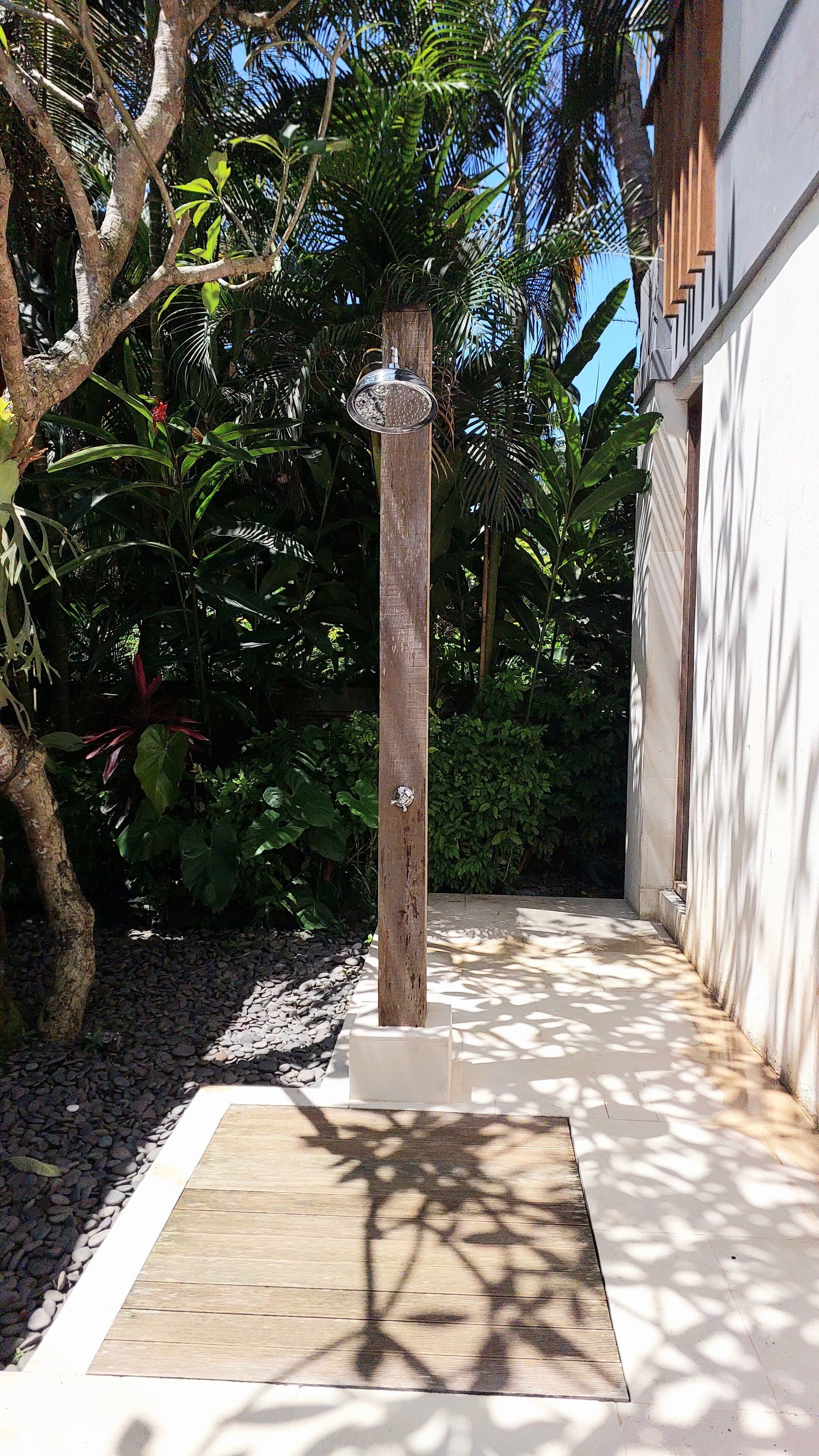 A pathway with a wooden deck, surrounded by lush greenery and a white building.