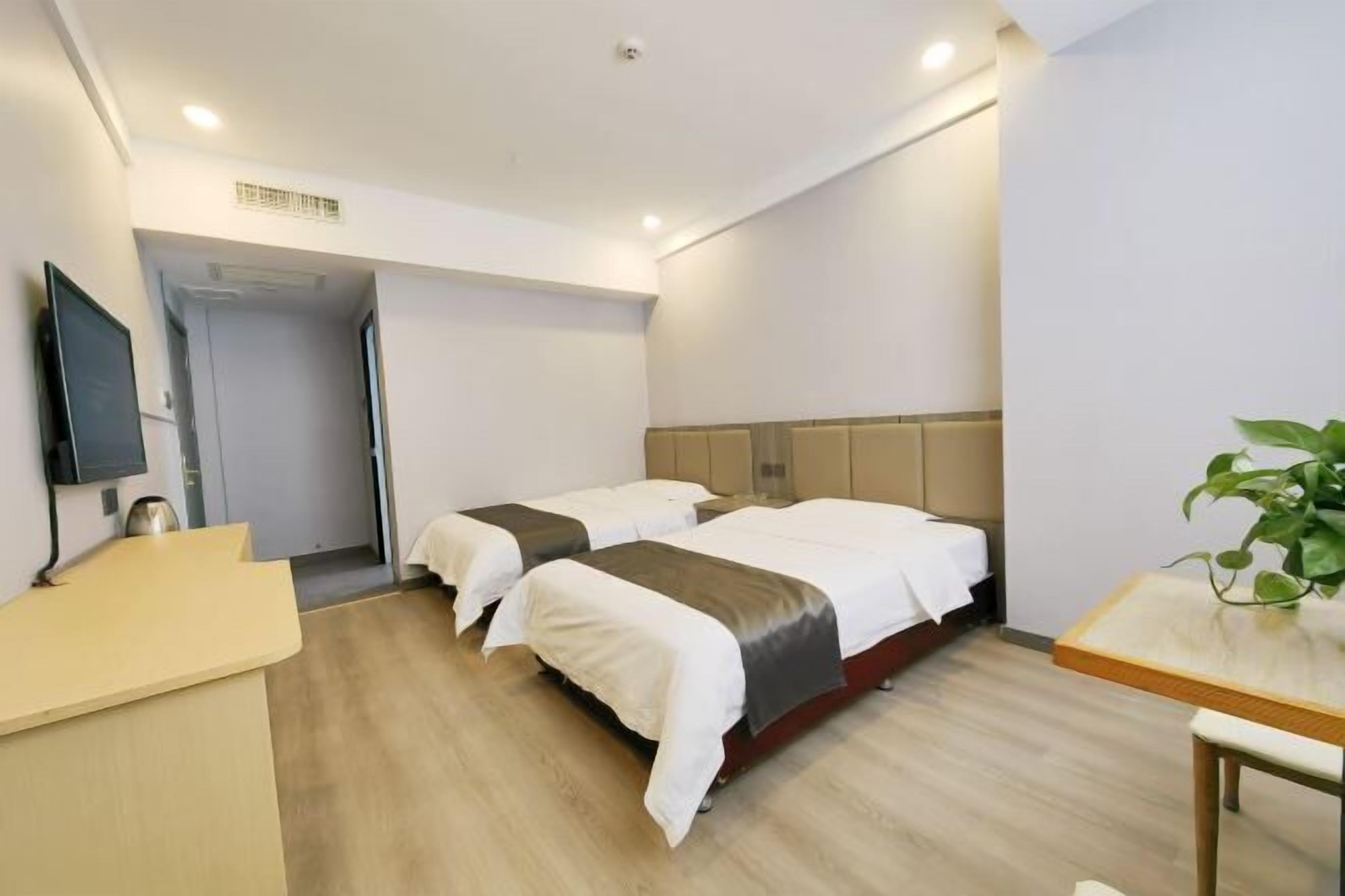 Ein Hotelzimmer mit zwei Betten, einem Schreibtisch, einem Fernseher und einer Pflanze.