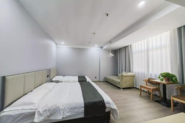 A modern hotel room with a large bed, a sofa, a small table with chairs, and a potted plant.