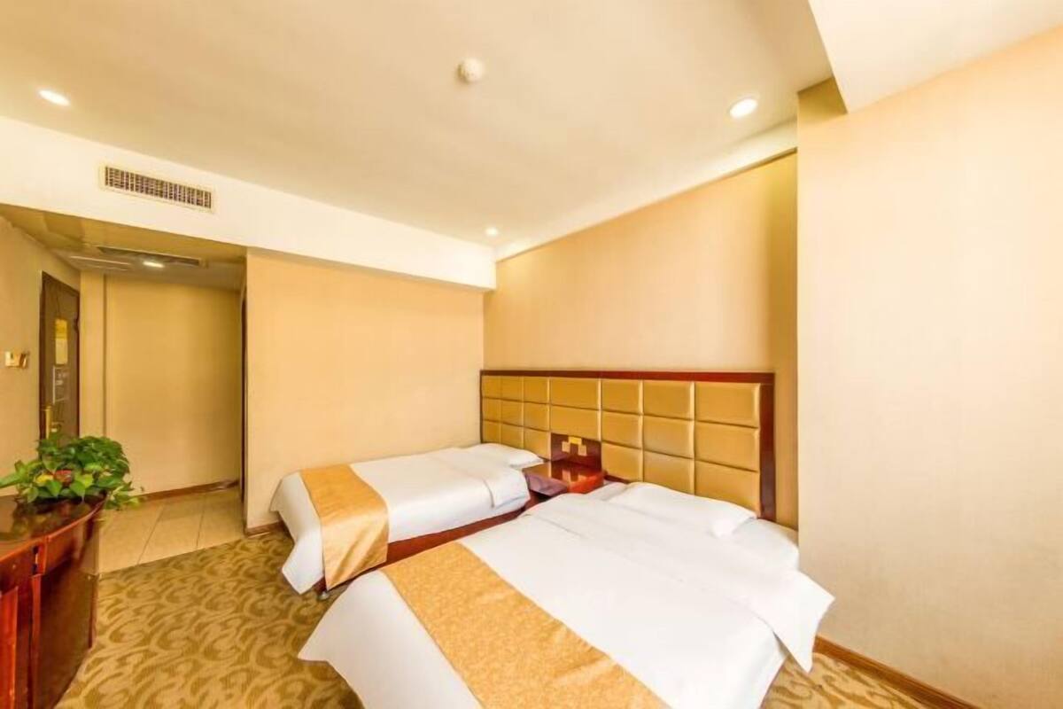 A hotel room with two beds, a desk, and a potted plant.