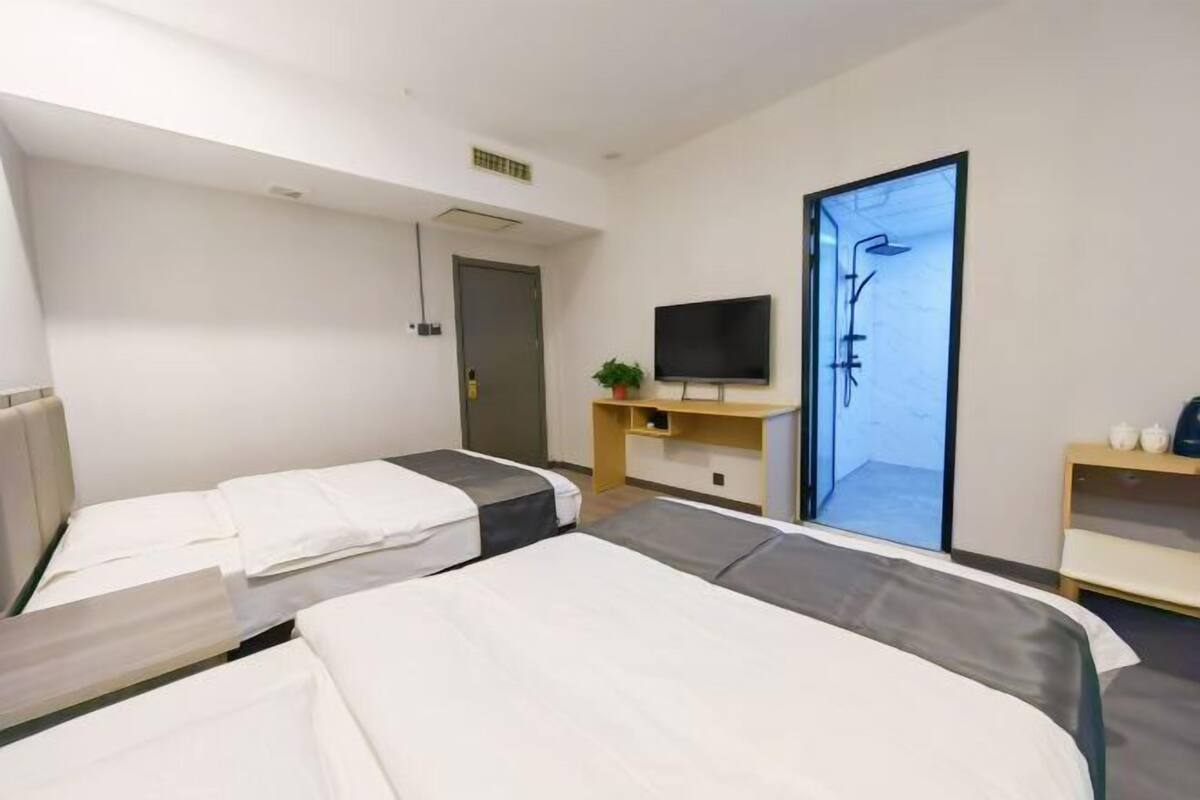A hotel room with two beds, a TV, a desk, and a shower area.