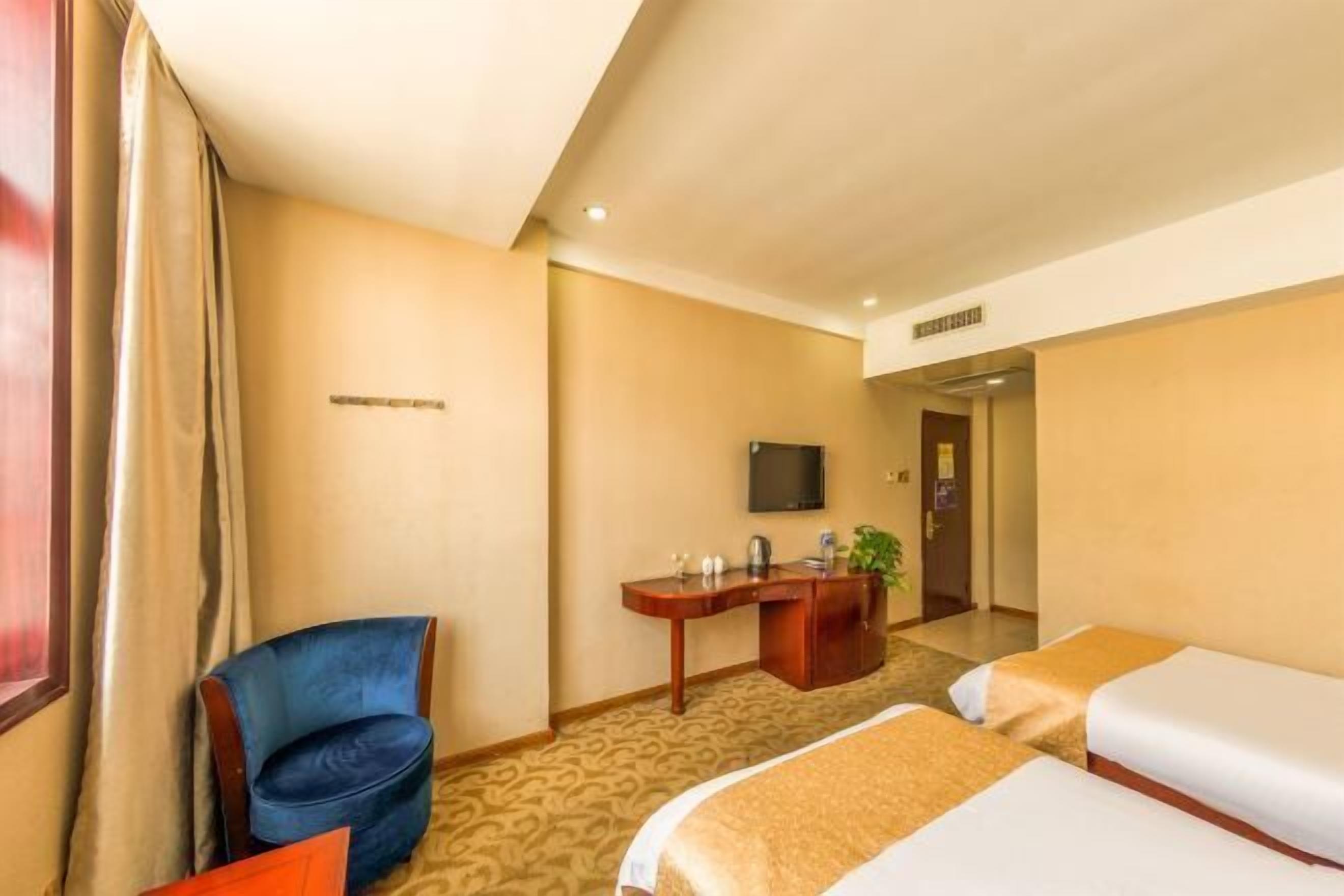 Habitació d'hotel amb dos llits, una escriptori amb un televisor, una cadira i una planta.
