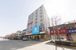 Un edificio de varios pisos con un llamativo letrero azul en la planta baja, probablemente indicando un hotel o restaurante. Se ven varios coches aparcados y un autobús al frente, lo que sugiere una calle con mucho tráfico.