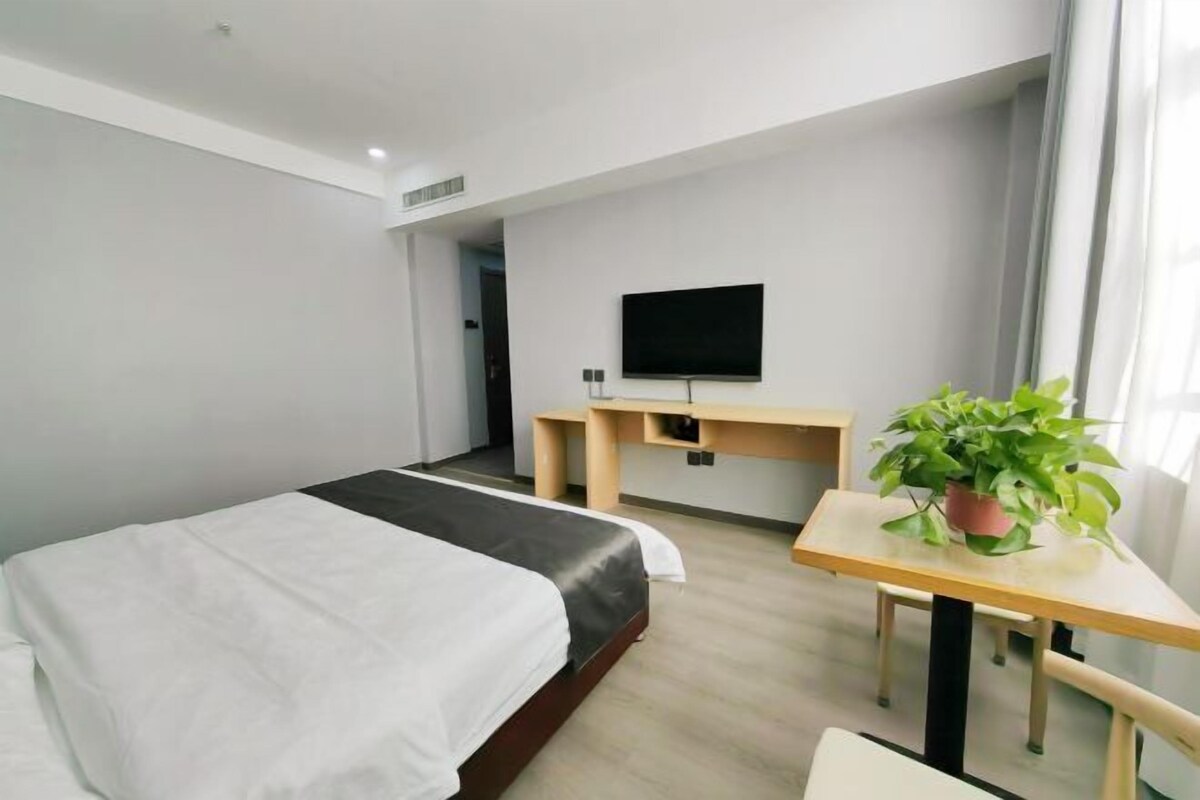 A modern hotel room with a bed, a desk, a television, and a potted plant.