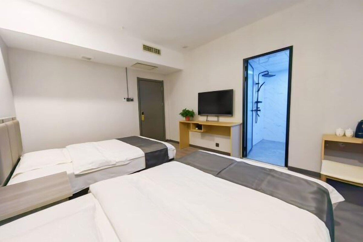 A hotel room with two beds, a TV, a desk, and a shower area.