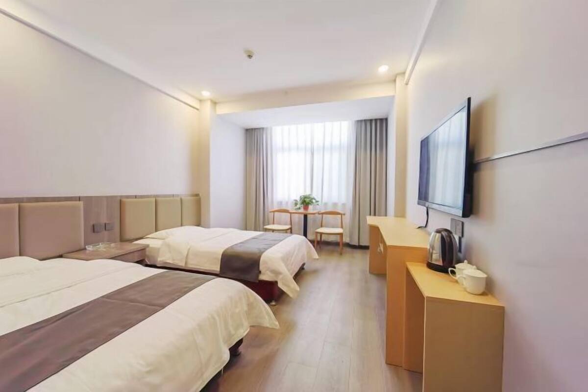 A hotel room with two beds, a desk, a television, and a window with curtains.