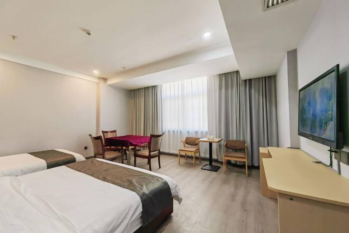 A hotel room with two beds, a desk, a chair, a small table, and a TV.