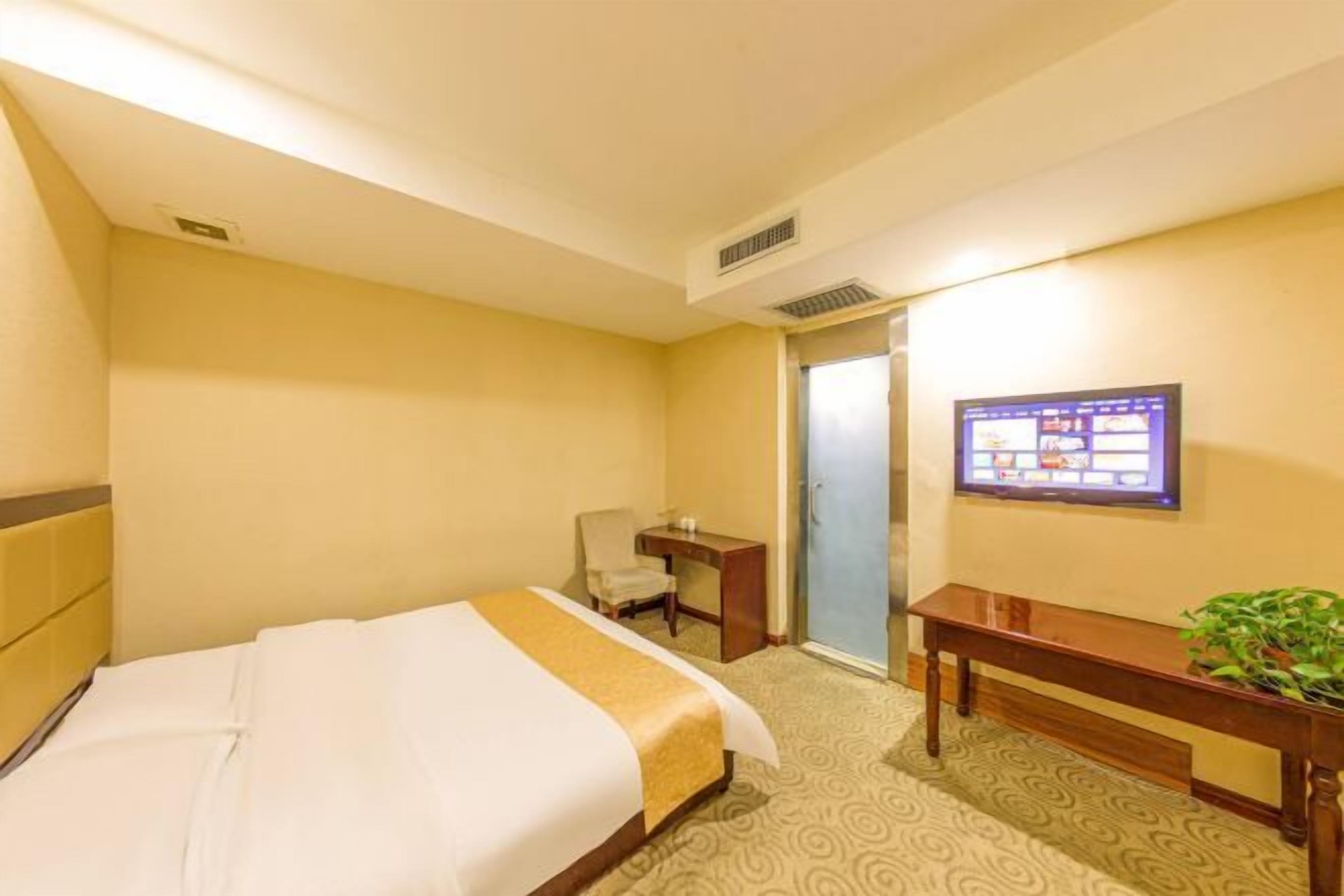 Une chambre d’hôtel avec un lit, un bureau, une chaise, une télévision et une porte.