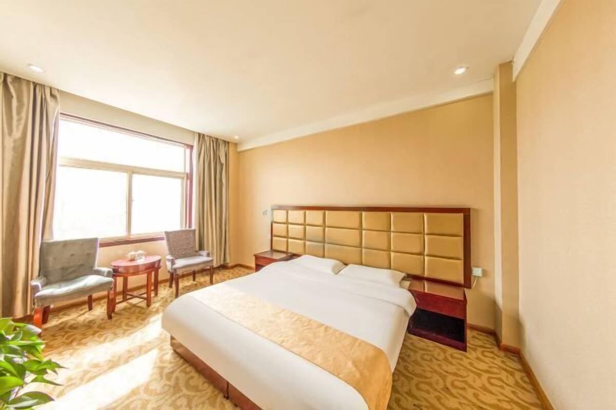 A hotel room with a large bed, two armchairs, a small table, and a window with curtains.