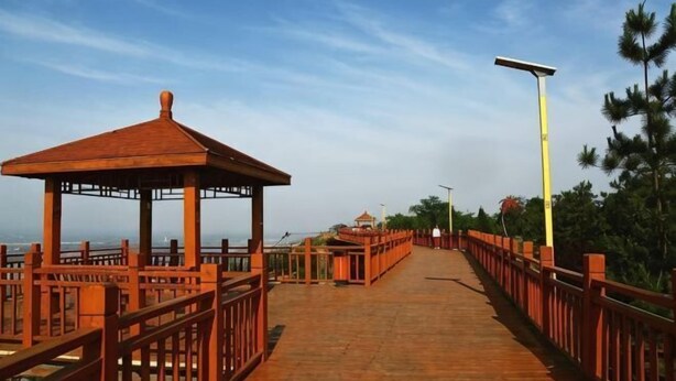 A wooden boardwalk with a gazebo, a street lamp, and trees in the background.
