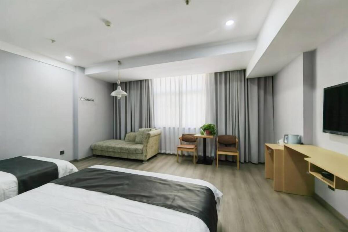 A hotel room with two beds, a desk, a chair, a sofa, and a TV.
