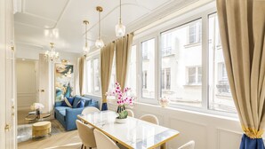 A spacious living room with a large window, a dining table, and a sofa. - Merveil - Luxury Suite - Marais - Poissonniere (Paris)