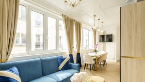 A modern living room with a blue sofa, a dining area with a table and chairs, and a large wooden cabinet. - Merveil - Luxury Suite - Marais - Poissonniere (Paris)