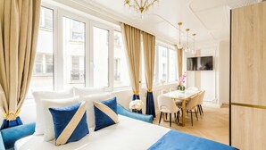 A hotel room with a large bed, a dining area, and a TV on the wall. - Merveil - Luxury Suite - Marais - Poissonniere (Paris)