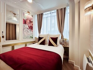 A hotel room with a large bed, a painting on the wall, and a window with curtains.