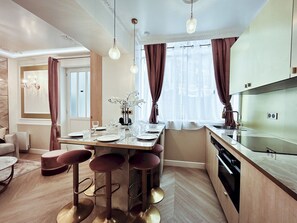 A modern kitchen with a dining area, bar stools, and a chandelier.