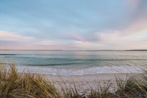 A beach with waves, grassy dunes, and a clear sky.