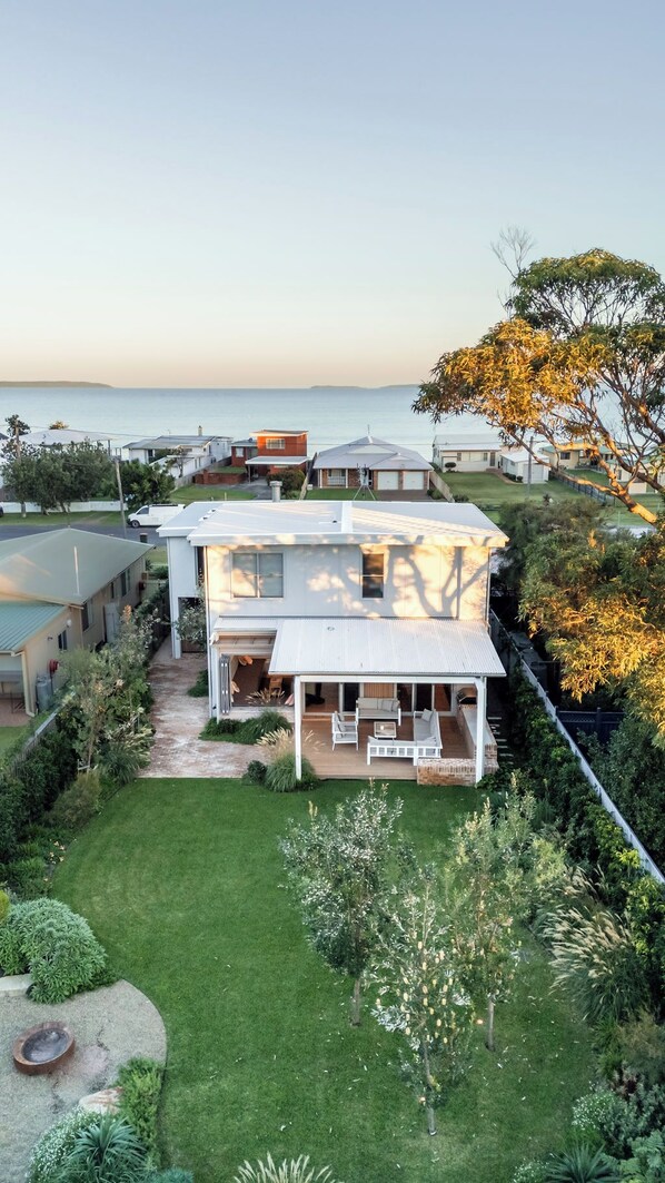 A residential property with a spacious backyard, a covered patio, and a view of the sea.