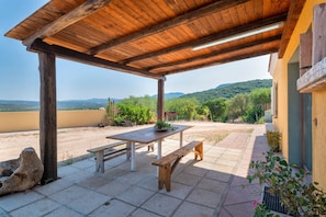 Patio esterno con pergolato in legno, tavolo e panche.